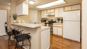 A kitchen with a central island, bar stools, a microwave, stove, and a refrigerator. - Adventurers Base Camp! (Boise)
