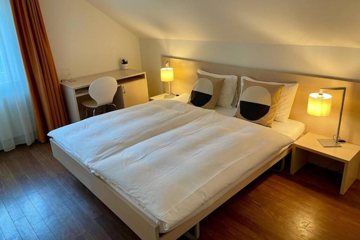A hotel room with a large bed, two bedside tables with lamps, a desk, and a chair.