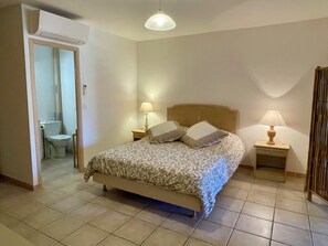 Ein Schlafzimmer mit einem Bett, zwei Nachttischen mit Lampen, einem hölzernen Kopfteil und einem durch eine offene Tür einsehbaren Badezimmer sowie einer Deckenleuchte.