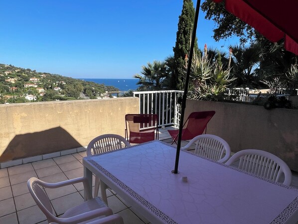 Eine Terrasse mit Tisch und Stühlen mit Blick auf eine Küstenlandschaft mit Häusern und wolkenlosem Himmel.