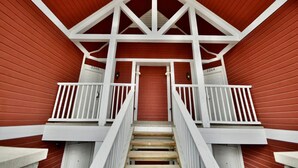 A red building with white railings and a staircase leading to a door.