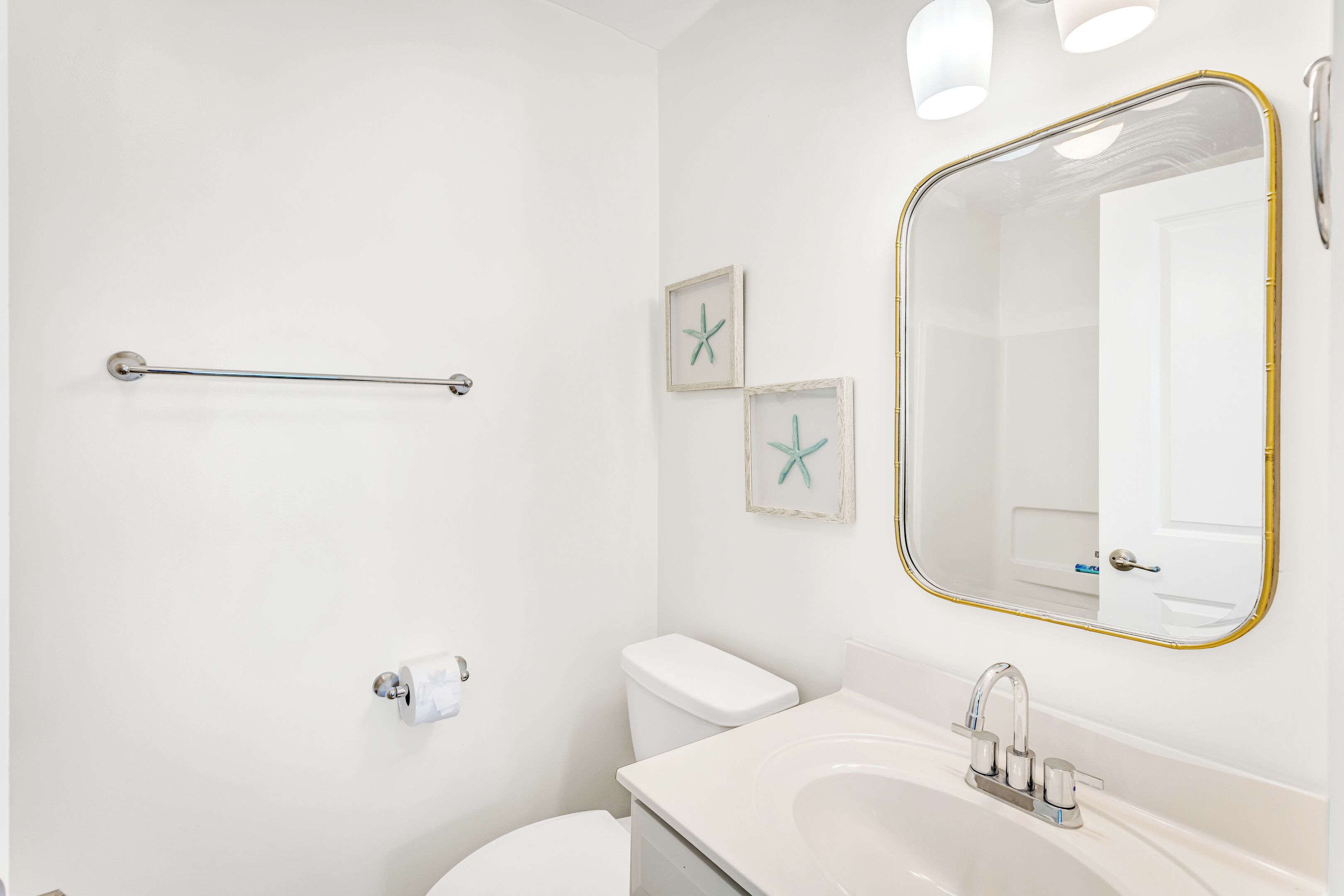 A bathroom with a toilet, sink, and mirror. There are starfish decorations on the wall and a towel rack.