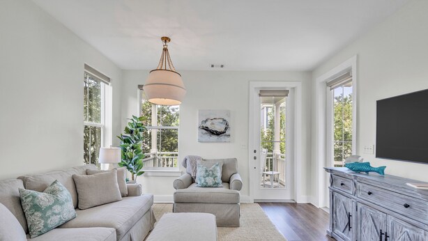 A spacious living room with a neutral color palette, a large window, and a modern chandelier.