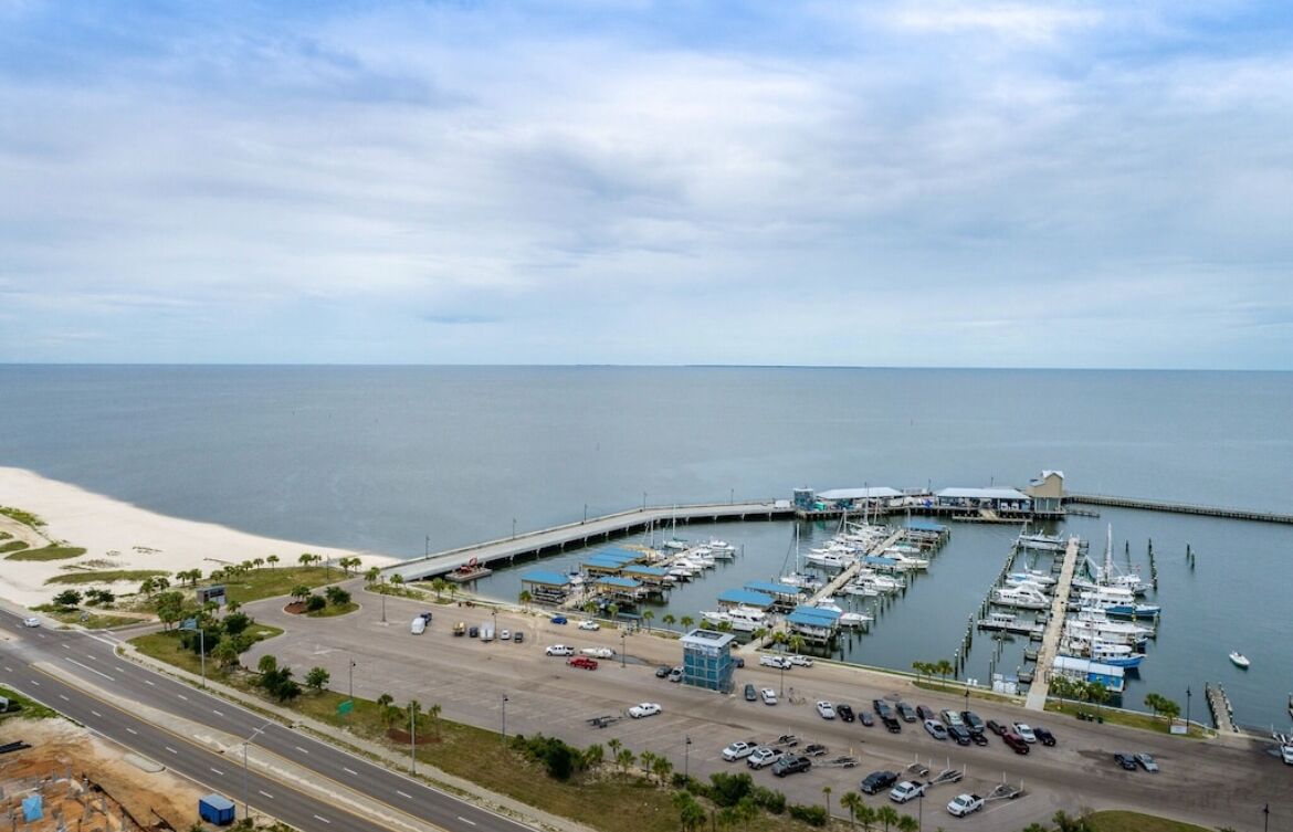 Un puerto deportivo con barcos amarrados, un estacionamiento y una carretera que conduce al puerto.