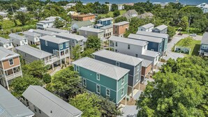 A residential area with multiple two-story houses, some with balconies, surrounded by greenery and a view of the ocean.