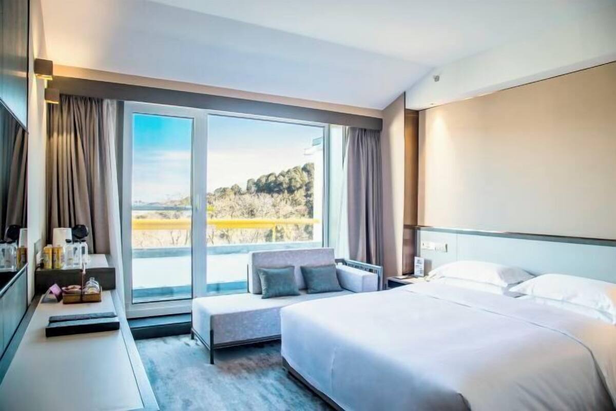 A hotel room with a large bed, a seating area by a window, and a desk with a lamp.