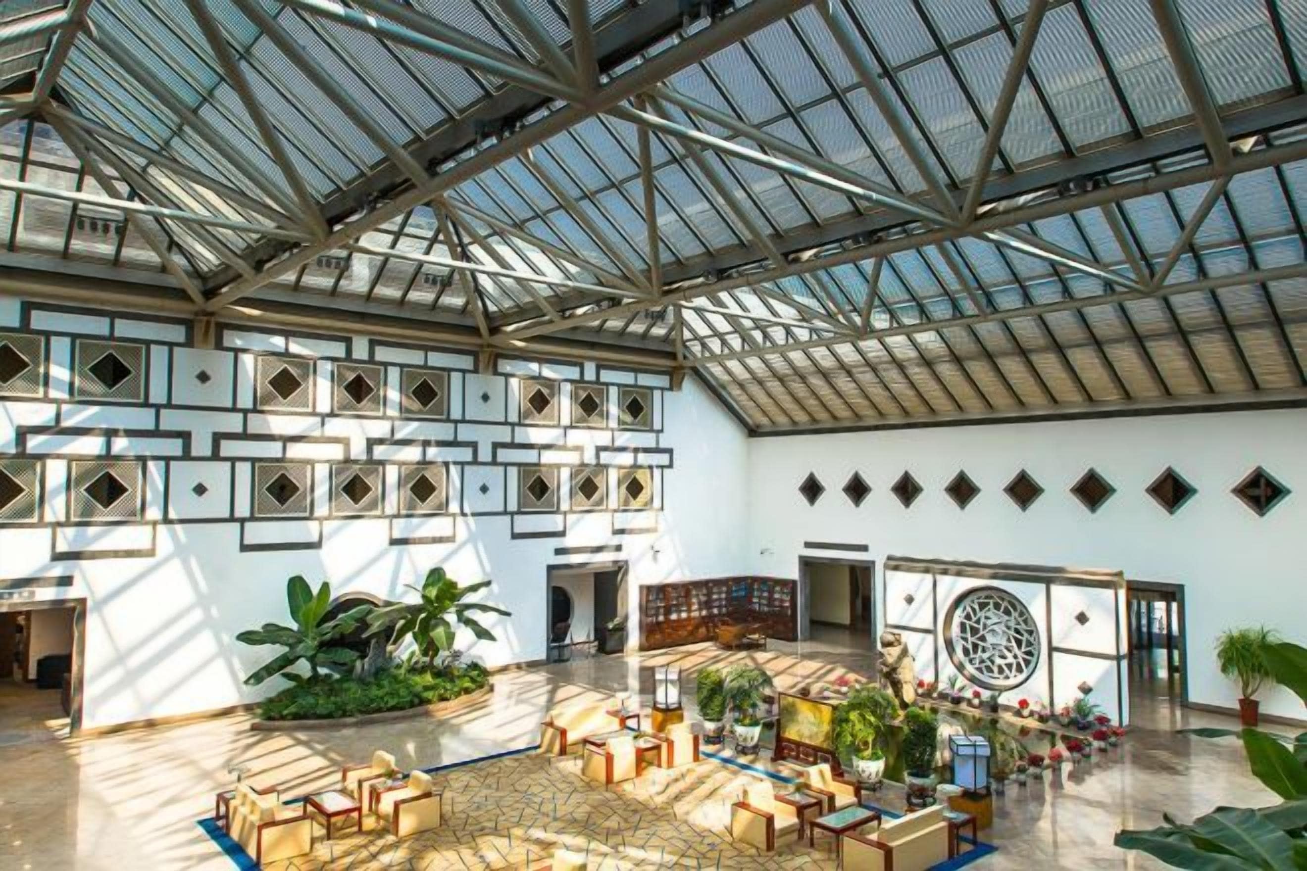 Een ruime atrium met een hoge plafond, grote ramen en een centraal zitgedeelte met tafels en stoelen.