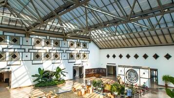 Een ruime atrium met een hoge plafond, grote ramen en een centraal zitgedeelte met tafels en stoelen.
