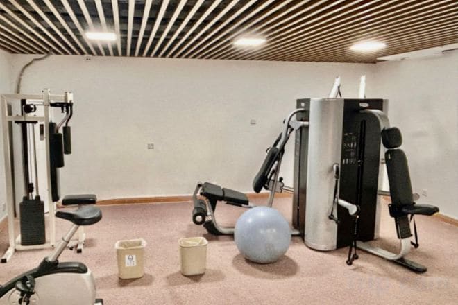 Un gimnasio con equipos de ejercicio variados, incluyendo una prensa de banca, una máquina de remo y una bicicleta estática.