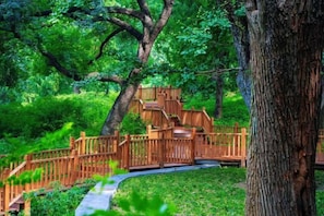 A wooden staircase leading up to a wooden deck surrounded by lush greenery. - Fragrant Hill Hotel (Beijing)