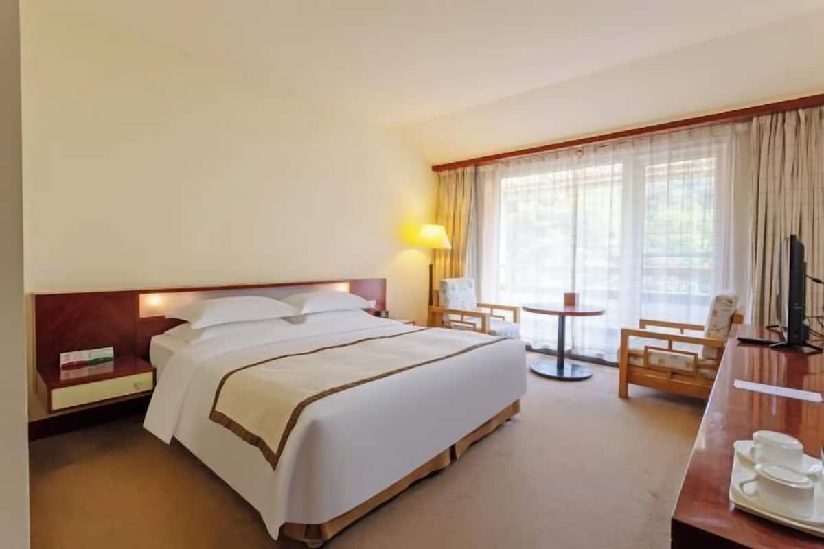 A hotel room with a bed, bedside table, lamp, chair, and a small table with cups.