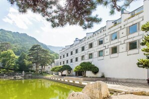 Un edificio tradicional con un patio, un estanque y montañas al fondo.