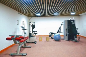 Un gimnasio con equipo de ejercicio, una máquina fijada a la pared y una pelota grande para ejercicio.