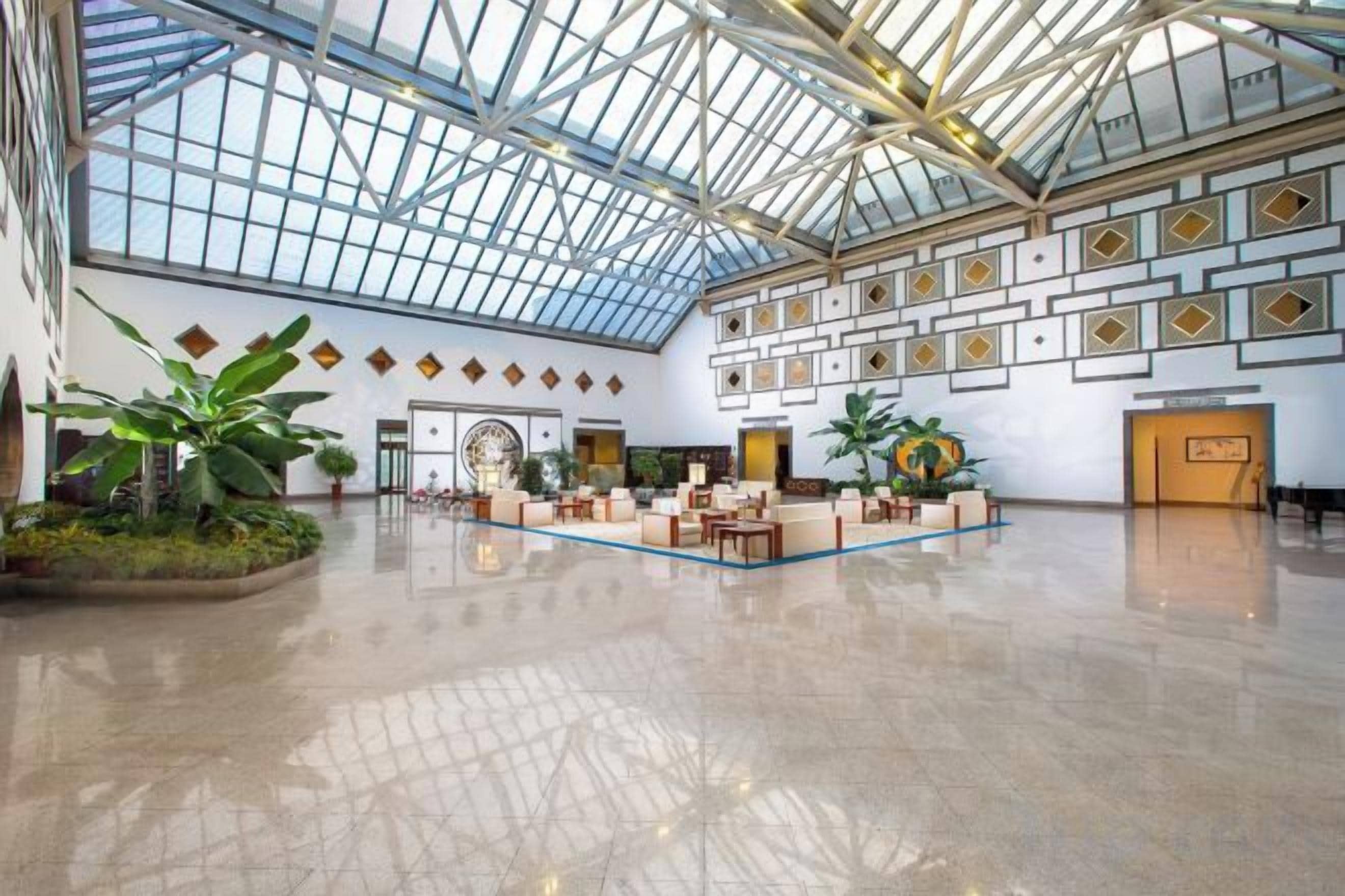 A spacious lobby with a high ceiling and a glass roof, featuring a central seating area and decorative wall panels.