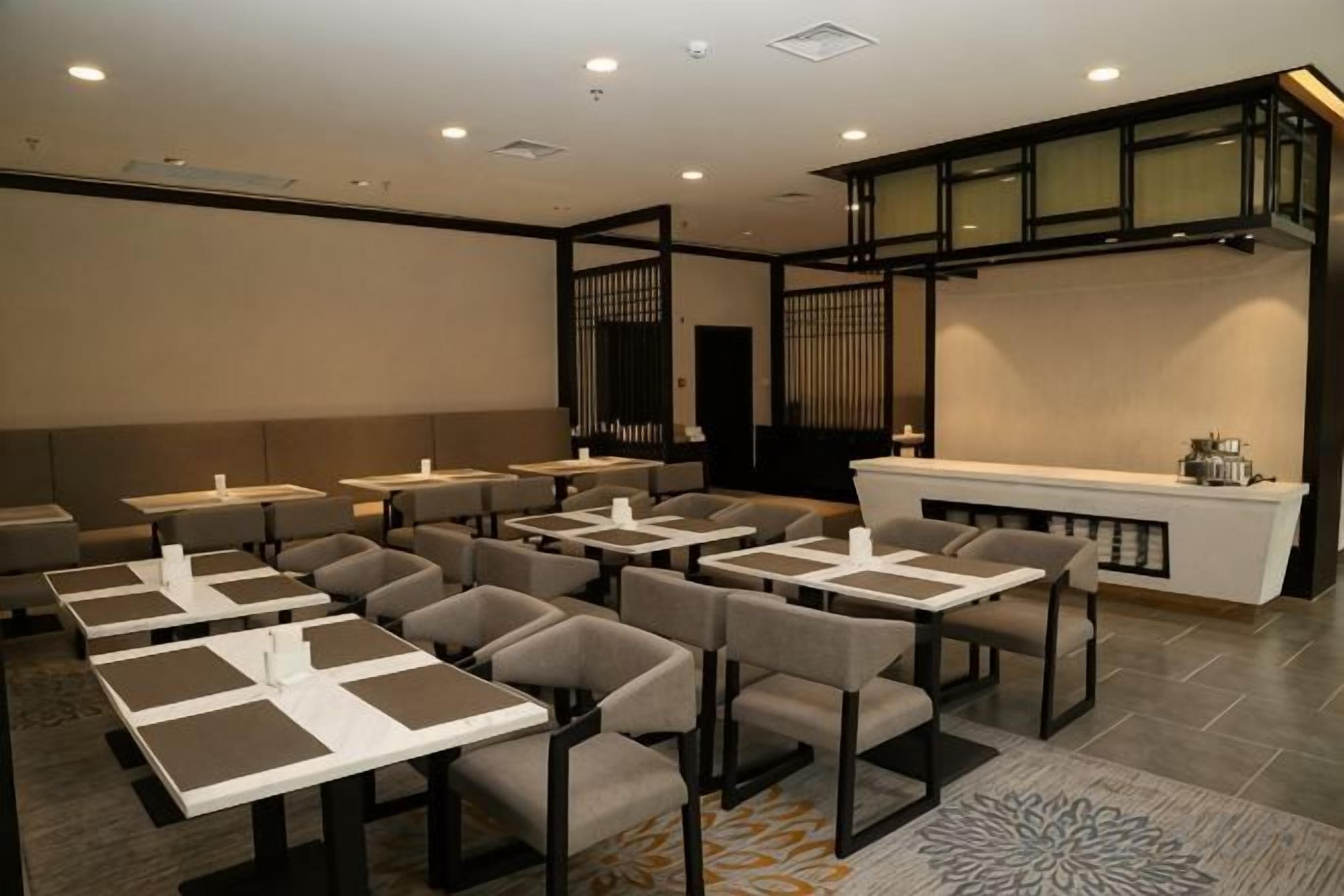 A hotel dining area with multiple tables and chairs, a reception desk, and a decorative wall.