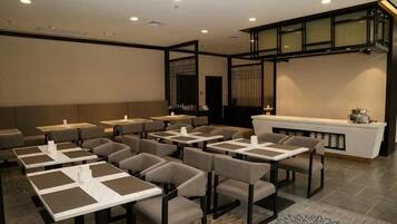 A hotel dining area with multiple tables and chairs, a reception desk, and a decorative wall.