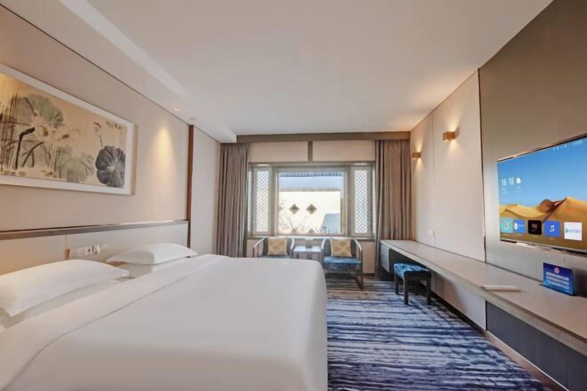 A hotel room with a bed, a desk, a TV, and a window with curtains.