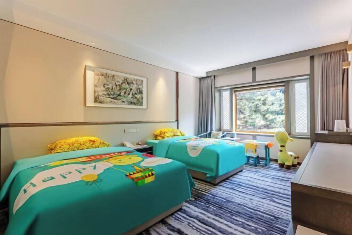 A hotel room with two beds, a desk, a chair, a window with a view, and a painting on the wall.