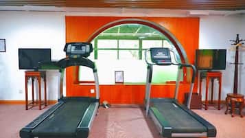 Una habitación con dos cintas de correr, un televisor sobre un pedestal y una ventana con marco anaranjado.