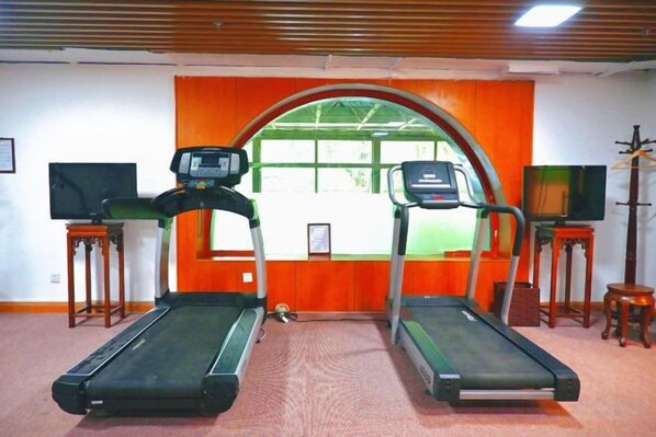 Une pièce équipée de deux tapis de course, d’un téléviseur posé sur un meuble et d’une fenêtre dont le cadre est orange.