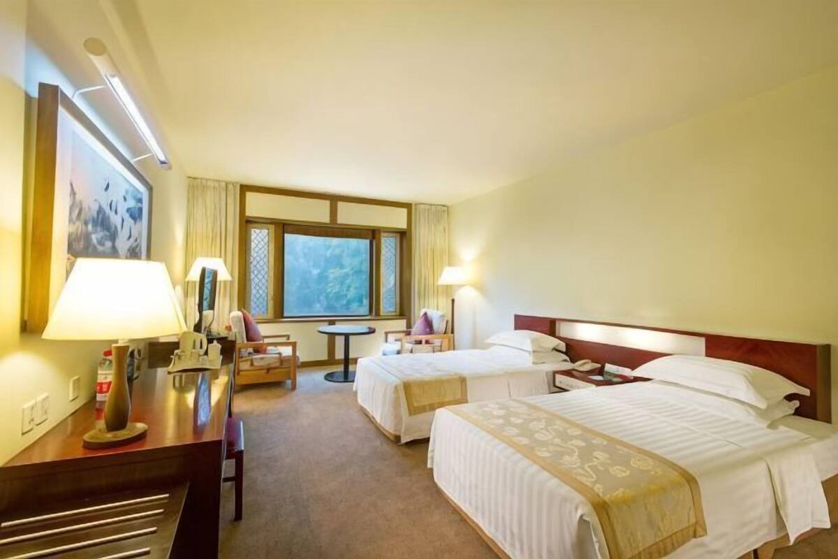 A hotel room with two beds, a desk, a chair, a small table, and a window.