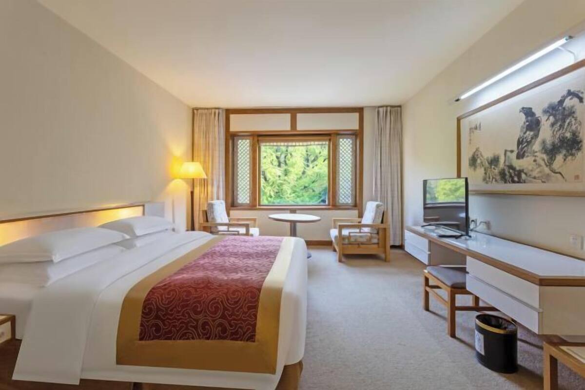 A hotel room with a bed, desk, chair, lamp, TV, and a window with a view.