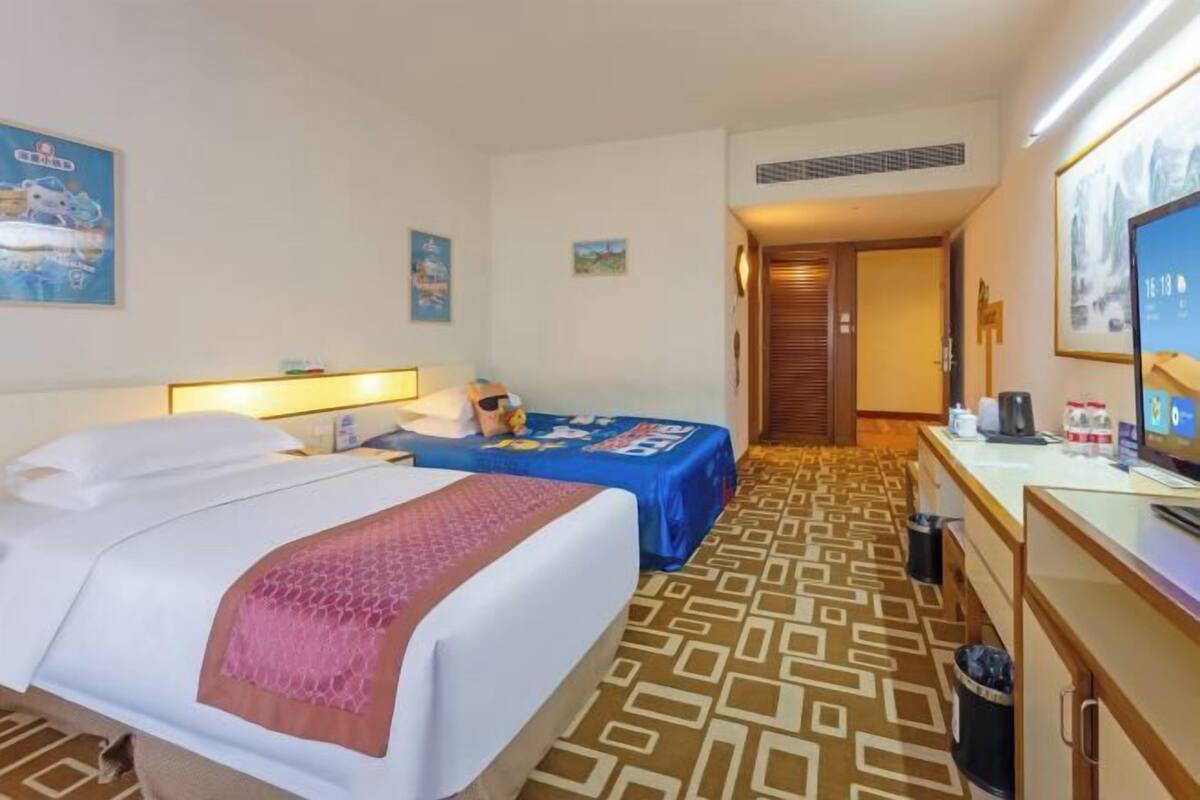 A hotel room with two beds, a desk with a computer, a TV, and a bathroom.