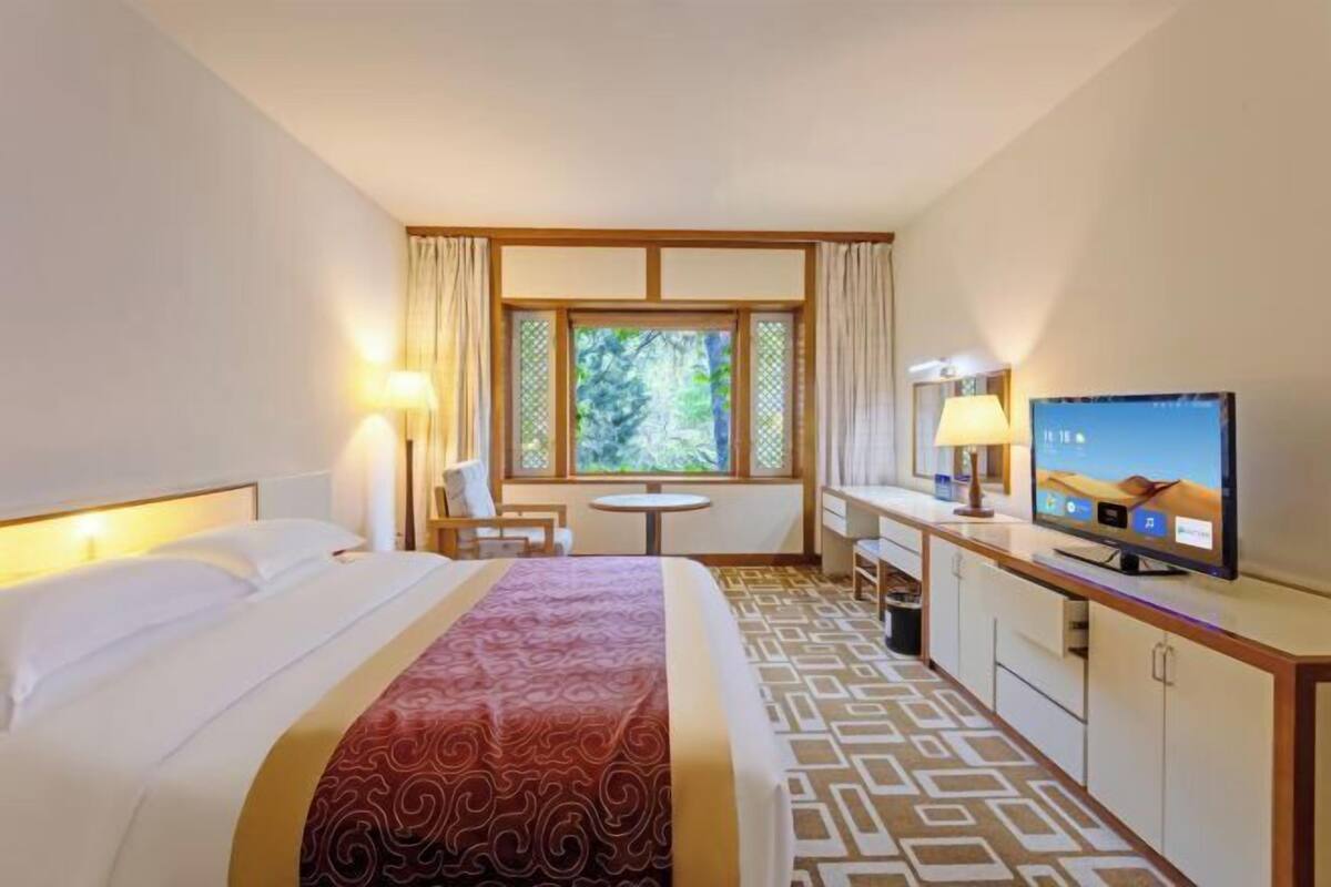 A hotel room with a bed, a TV, a desk, a chair, and a window with curtains.