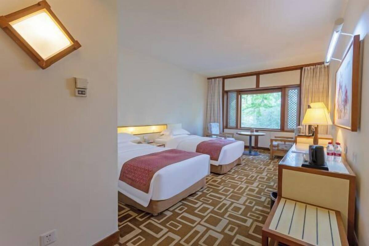 A hotel room with two beds, a desk, a chair, a window with curtains, and a patterned carpet.