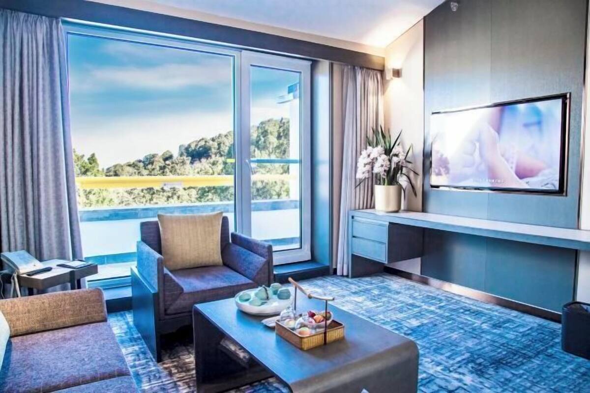 A modern hotel room with a large window offering a scenic view, a comfortable seating area, a flat-screen TV, and a small side table.