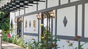 En modern byggnadsfasad med geometriska mönster, dekorativa vägglampor och en gångbana av betong med inslag av grönska.
