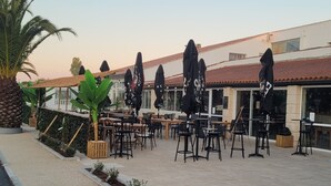 An outdoor seating area with tables and chairs, surrounded by potted plants and umbrellas. - Mobil Home 6 Personnes île D'oléron : Notre Oléronaise (Saint-Denis-d'Oléron)