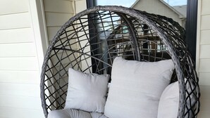Une chaise en osier avec des coussins, placée sur une terrasse en bois.