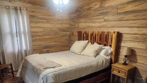 Une chambre à coucher de style cabane en bois, avec un lit, une table de chevet, une lampe et un tapis à carreaux.