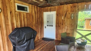 Une véranda couverte avec un barbecue, des fauteuils en osier et une porte blanche.