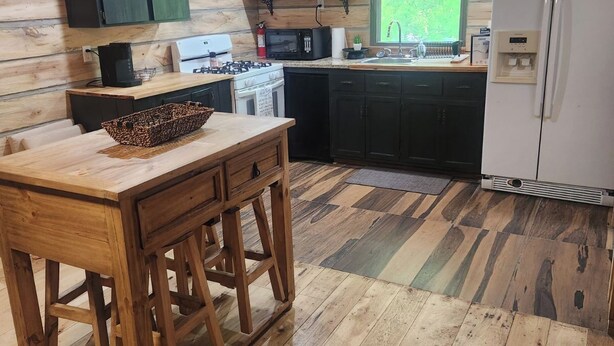 Une cuisine rustique avec un plancher en bois, une table en bois et un réfrigérateur.