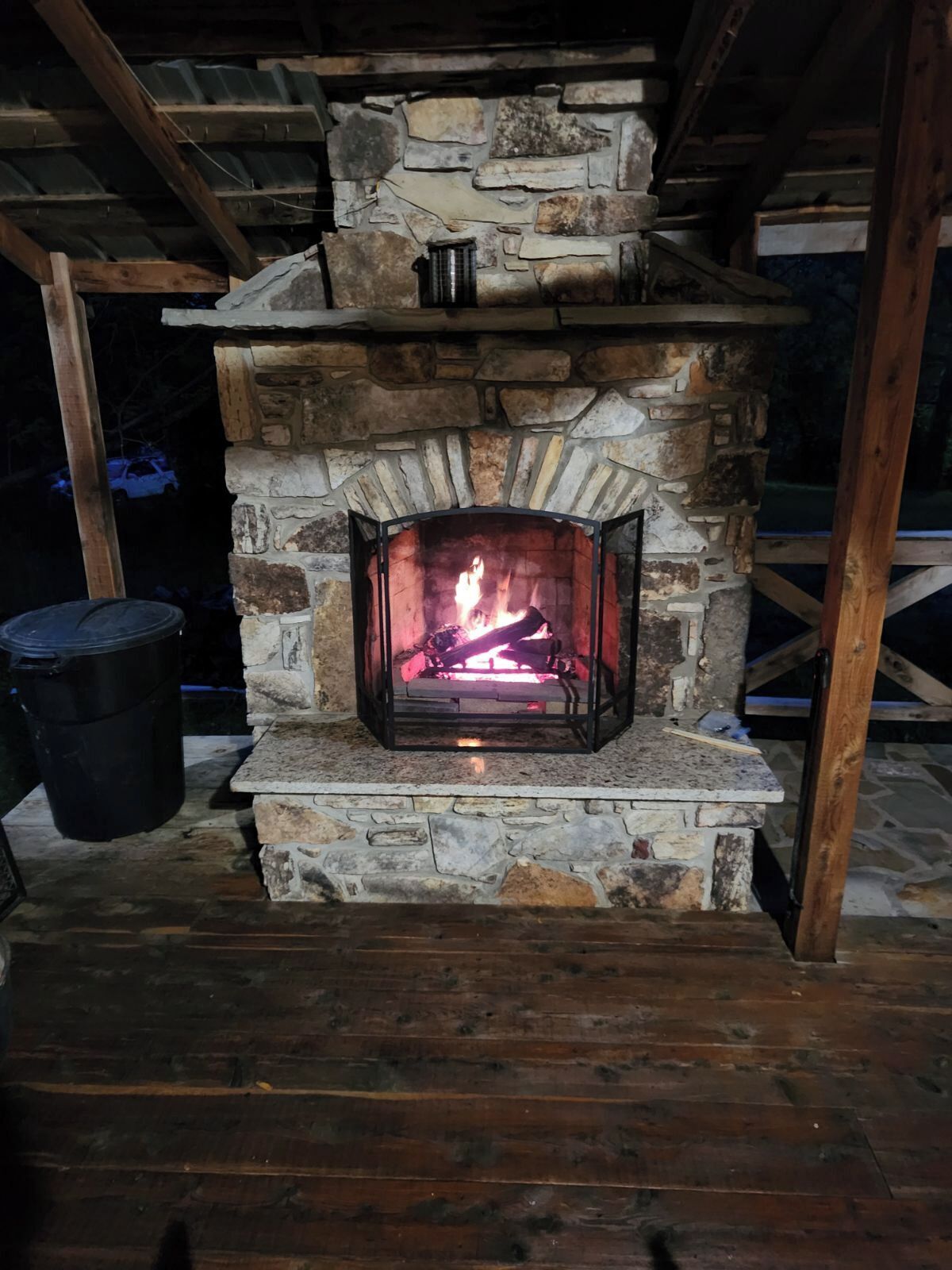 Ein Steinkamin mit brennendem Feuer, umgeben von Holzbalken und einem Steinfußboden.