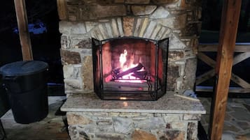 A stone fireplace with a fire burning inside, surrounded by wooden beams and a stone floor.