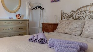 Un letto rifatto con asciugamani arrotolati, una cassettiera con decorazioni floreali e un letto con cuscini a motivi floreali.