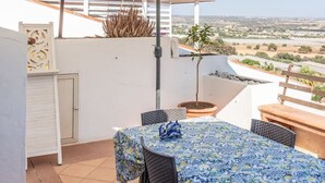 Un patio con tavolo e sedie, riparato da un ombrellone bianco, e vista sul paesaggio.