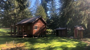 A rustic cabin with a porch, surrounded by a grassy area and dense forest. - Tranquil cabin with WiFi in Brush Prairie (Brush Prairie)