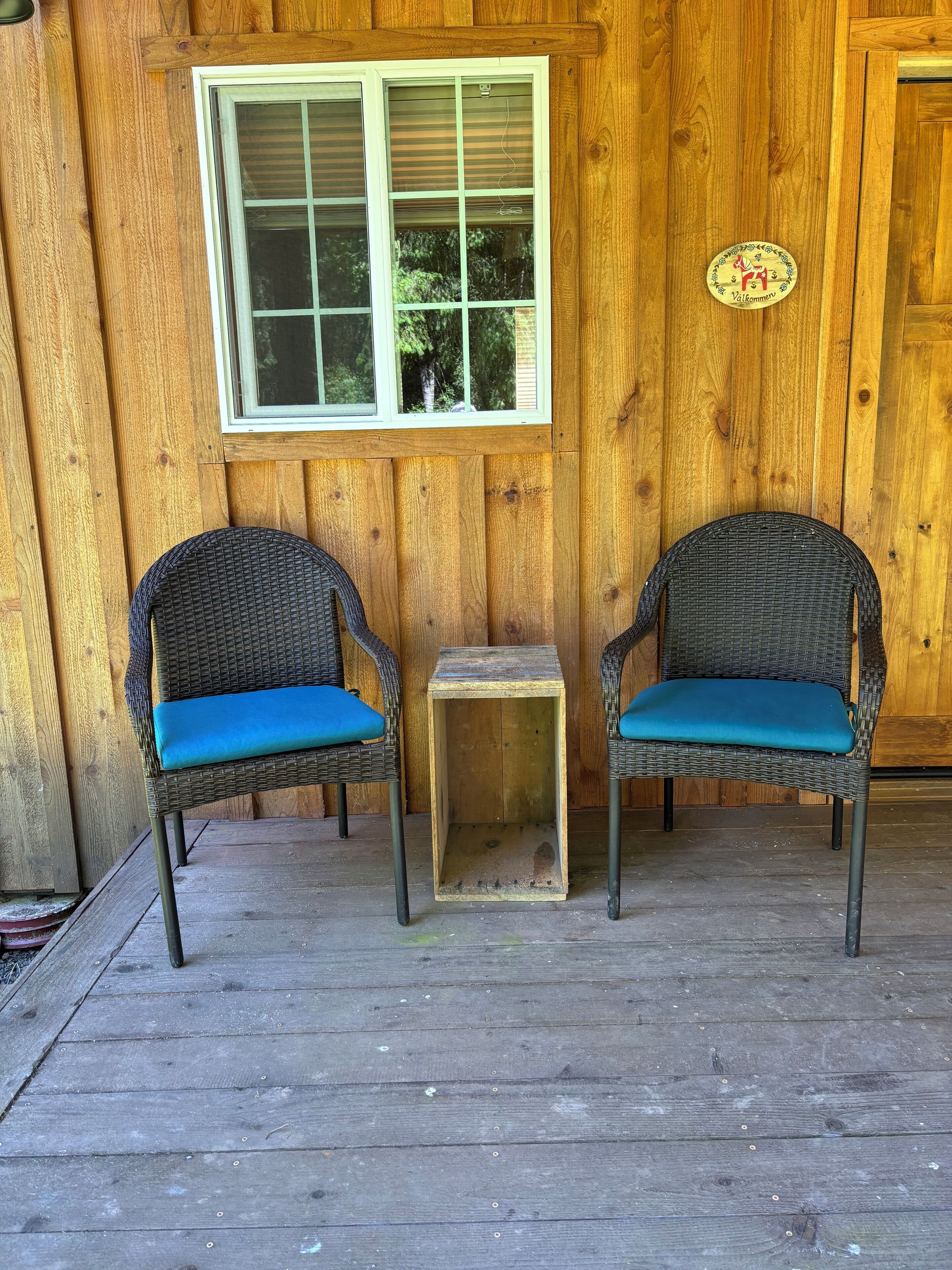 A wooden porch with two wicker chairs and a small table.