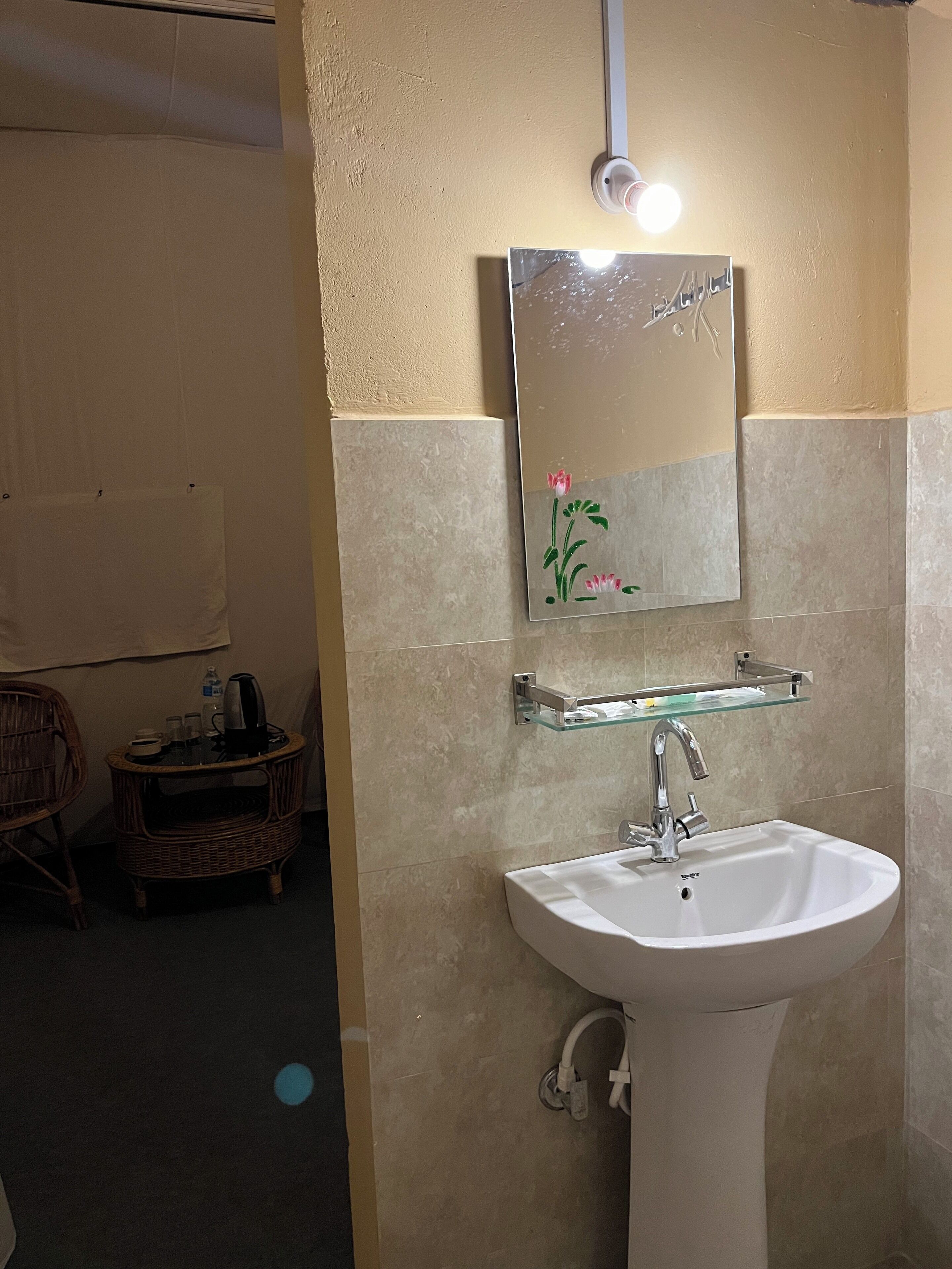 Et badeværelse med en hvid vask, en glasshylde over og et spejl med blomstermotiv.
