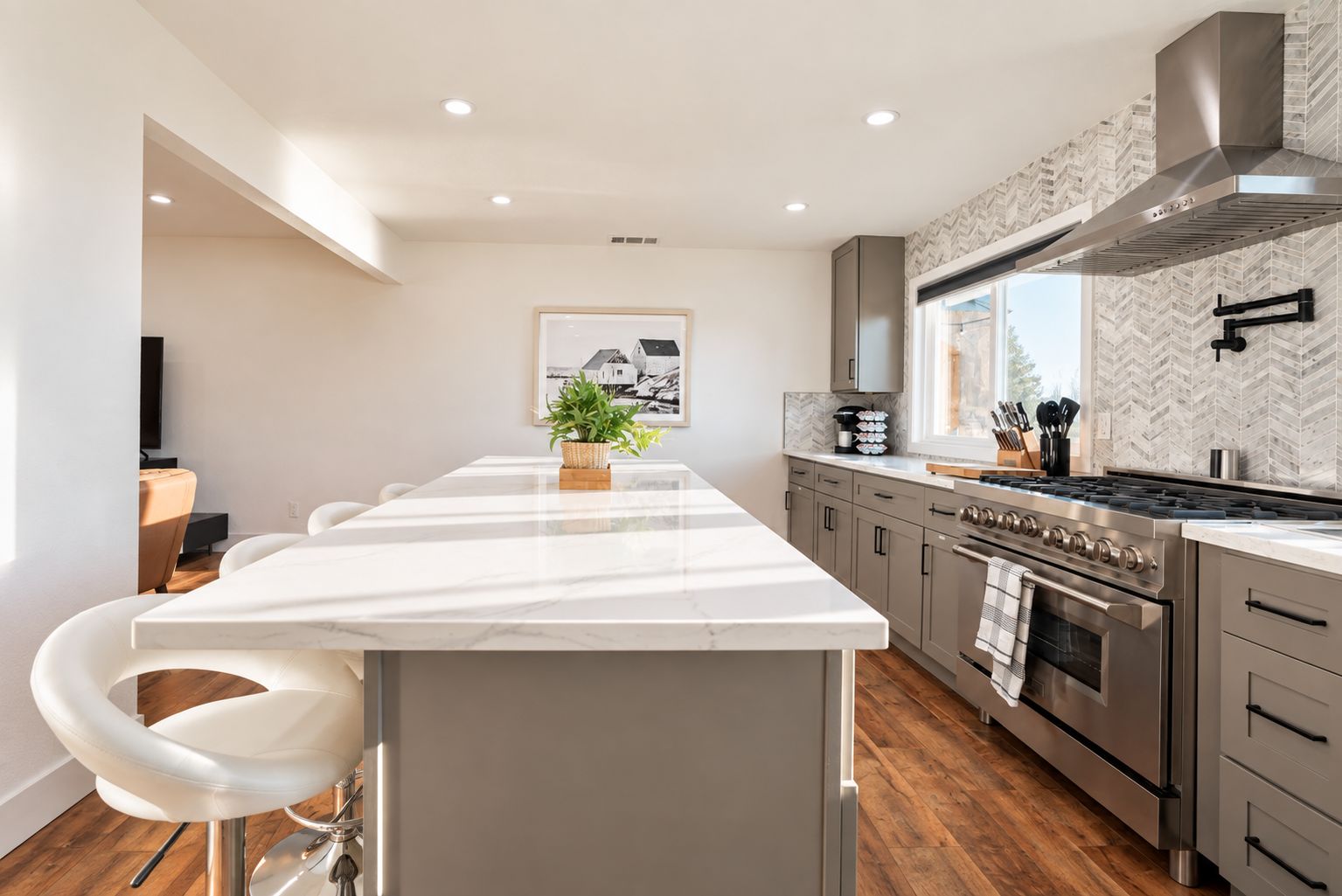 A modern kitchen with a central island, stainless steel appliances, and a herringbone-patterned backsplash.