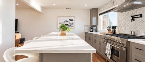 A modern kitchen with a central island, stainless steel appliances, and a herringbone-patterned backsplash.