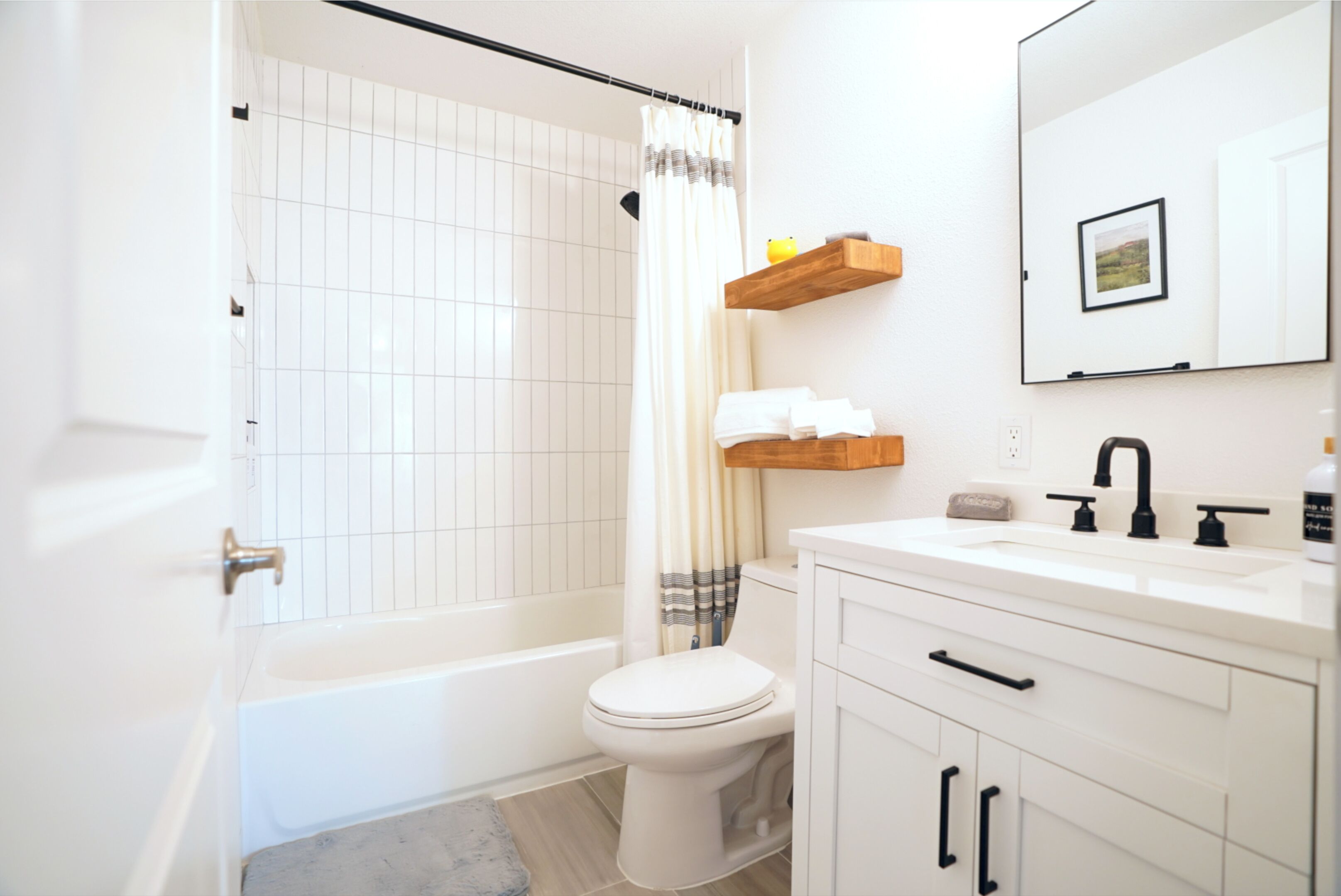 A modern bathroom with a bathtub, toilet, and white vanity with black handles.