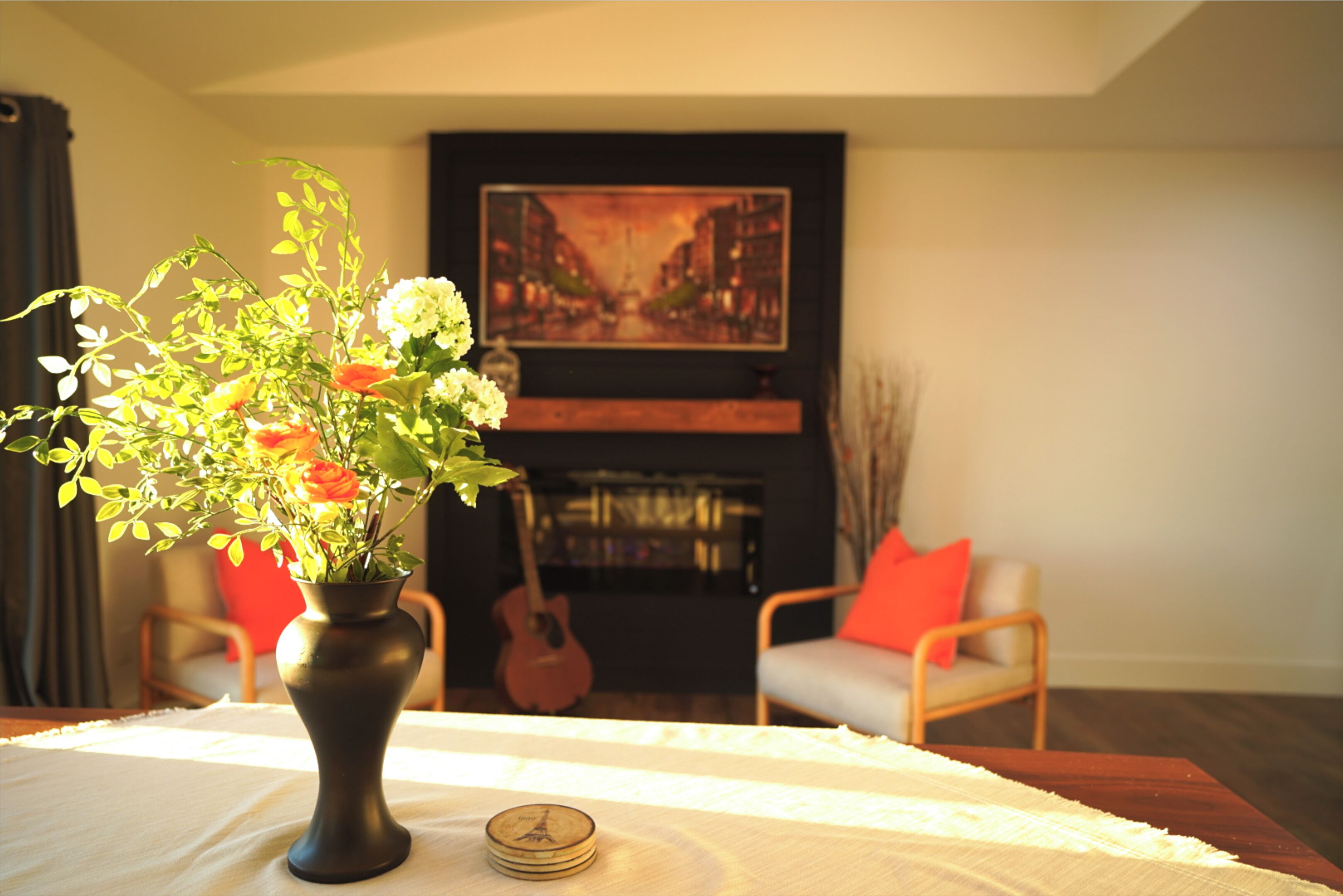 Un salon avec un vase de fleurs sur une table, une guitare et un tableau accroché au mur.