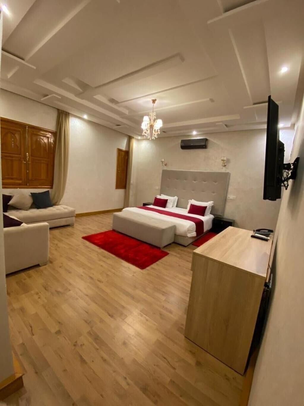 Une chambre moderne avec un grand lit, un canapé, une armoire en bois et un lustre.