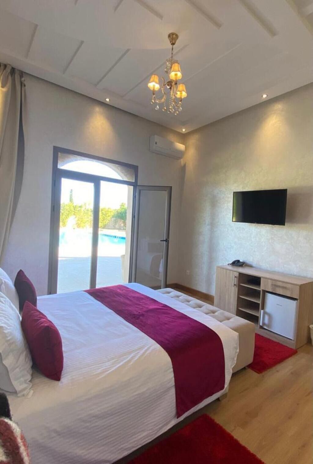 Een slaapkamer met een bed, een televisie, een bureau en een schuifdeur naar buiten.
