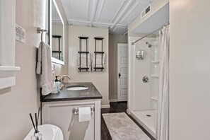 A bathroom with a sink, mirror, towel rack, shower, and a white door.